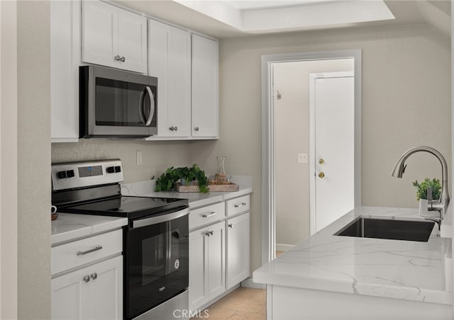 kitchen featuring appliances with stainless steel finishes, white cabinets, a sink, and light stone counters