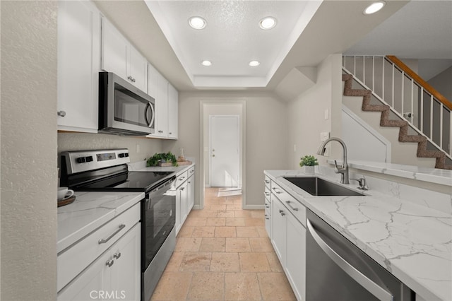 kitchen featuring stainless steel appliances, recessed lighting, stone tile flooring, a raised ceiling, and a sink