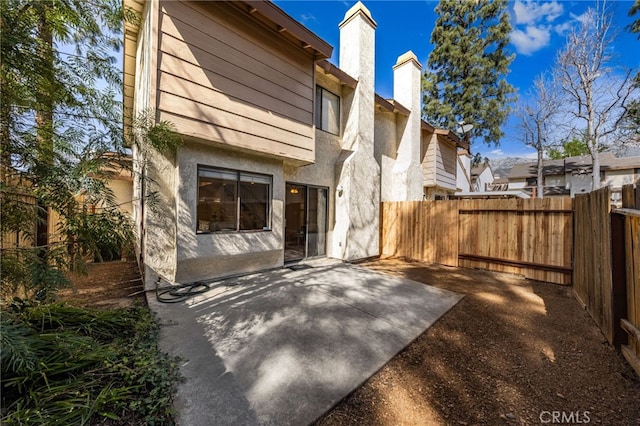 rear view of house with stucco siding, a fenced backyard, a chimney, and a patio