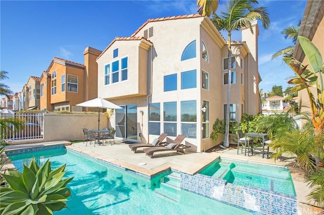 rear view of house featuring a pool with connected hot tub, fence, a tiled roof, stucco siding, and a patio area