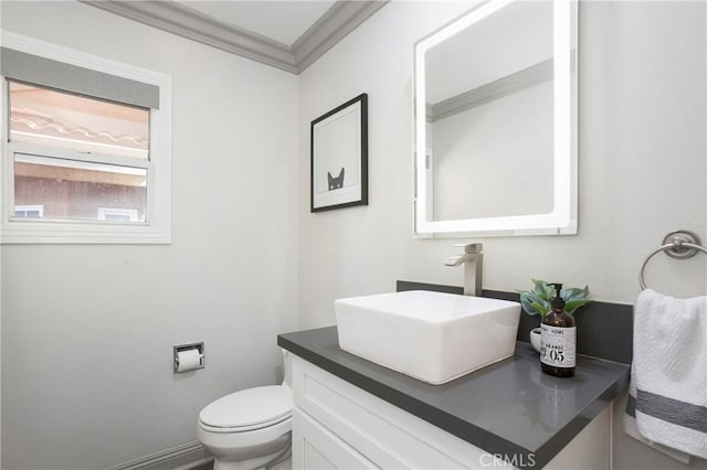 half bath with baseboards, toilet, ornamental molding, and vanity