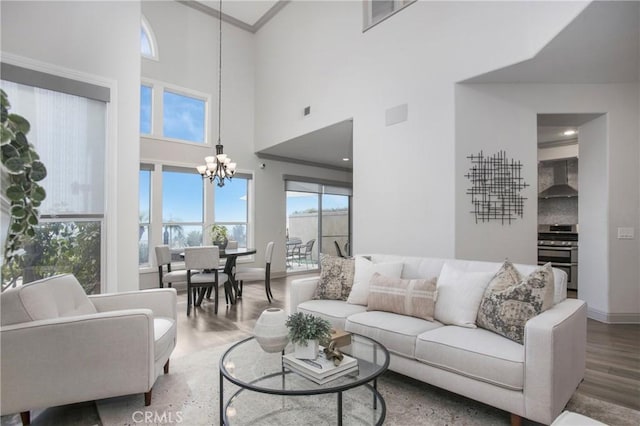 living room with crown molding, baseboards, wood finished floors, a towering ceiling, and an inviting chandelier