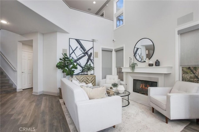 living area featuring stairway, recessed lighting, a high ceiling, wood finished floors, and a glass covered fireplace