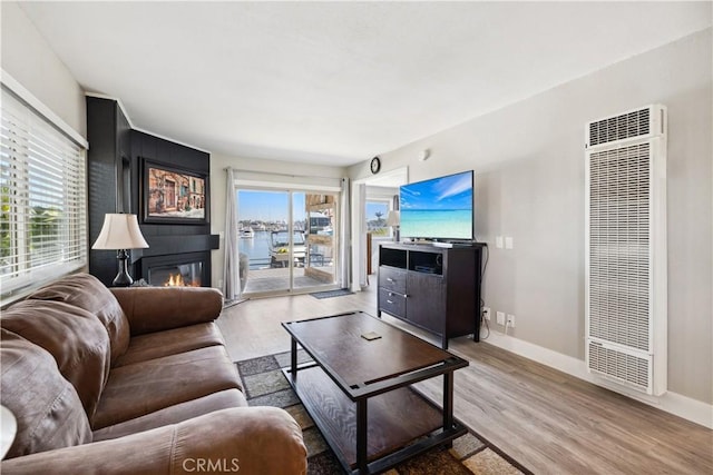 living room featuring a glass covered fireplace, a heating unit, baseboards, and wood finished floors