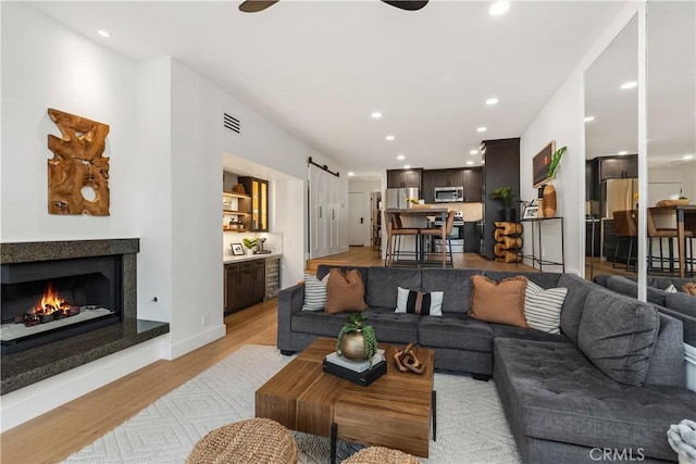 living area with a barn door, light wood-style flooring, recessed lighting, a fireplace, and visible vents