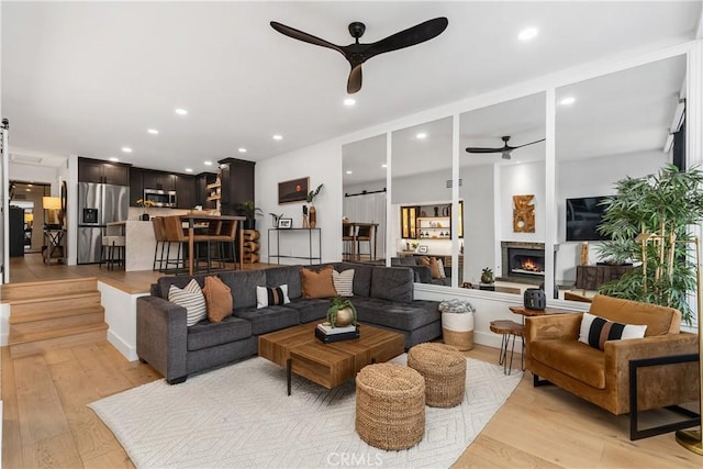 living area featuring a lit fireplace, light wood finished floors, a ceiling fan, and recessed lighting