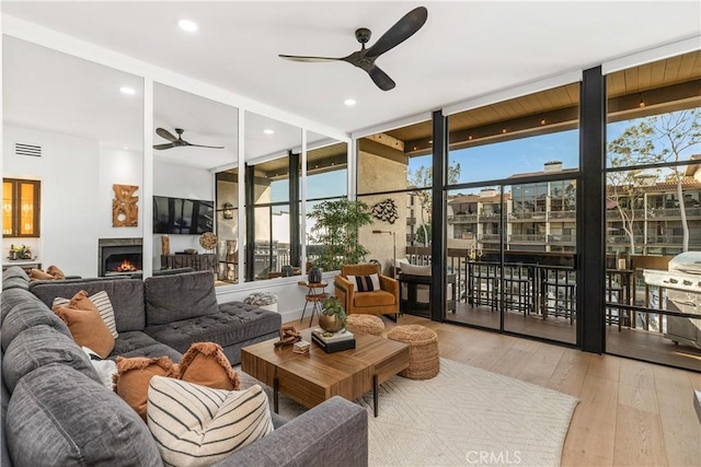 living area featuring a warm lit fireplace, visible vents, ceiling fan, and hardwood / wood-style floors