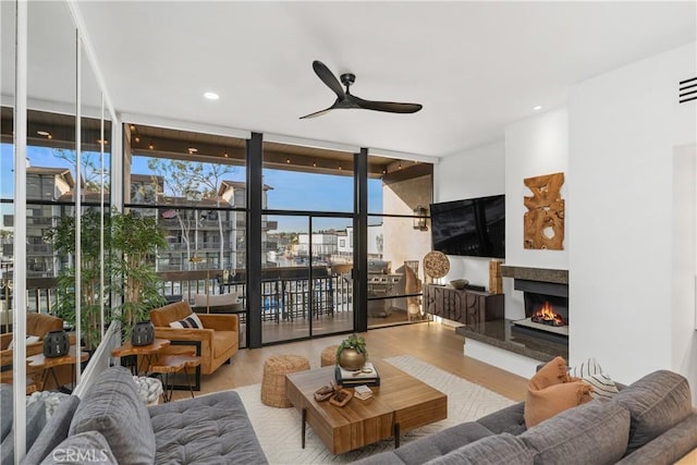 living area with recessed lighting, expansive windows, ceiling fan, wood finished floors, and a lit fireplace