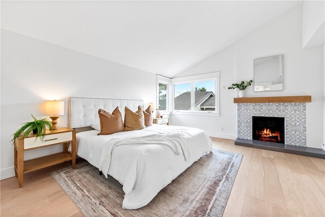 bedroom featuring lofted ceiling, light wood-style flooring, baseboards, and a tiled fireplace