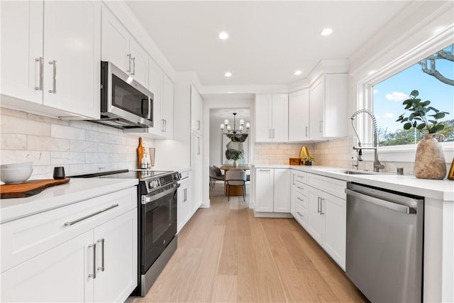 kitchen with tasteful backsplash, white cabinets, stainless steel appliances, light countertops, and light wood-style floors