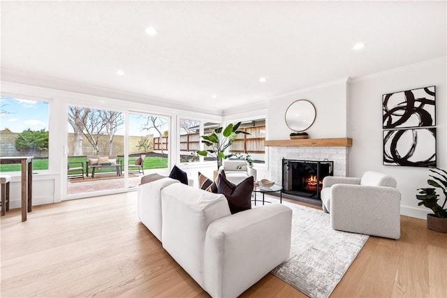 living area featuring ornamental molding, light wood-type flooring, a brick fireplace, and recessed lighting