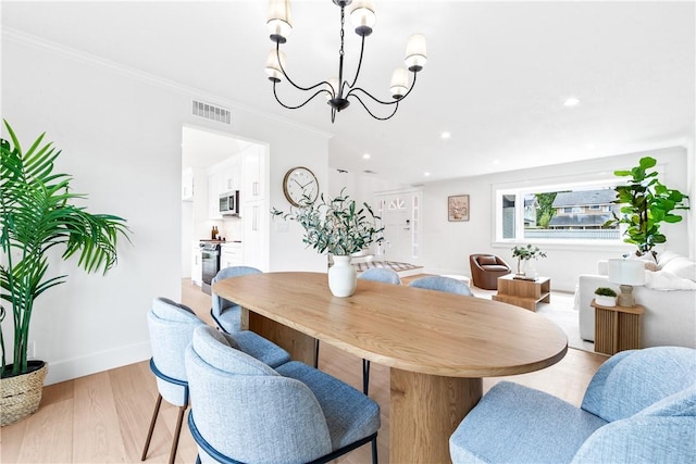 dining space featuring visible vents, baseboards, crown molding, light wood-style floors, and a notable chandelier