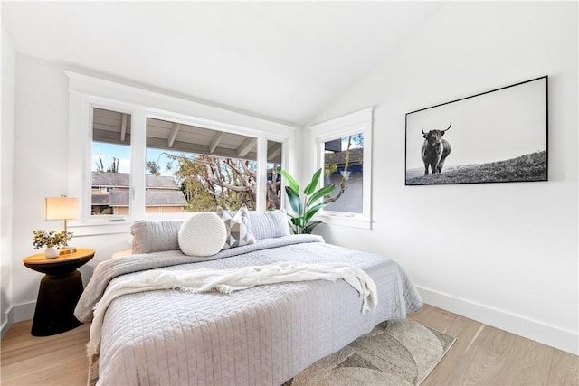 bedroom featuring lofted ceiling, multiple windows, baseboards, and wood finished floors