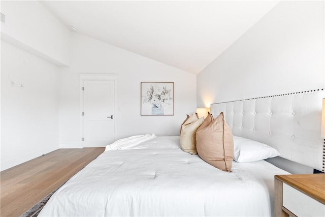 bedroom featuring visible vents, vaulted ceiling, baseboards, and wood finished floors