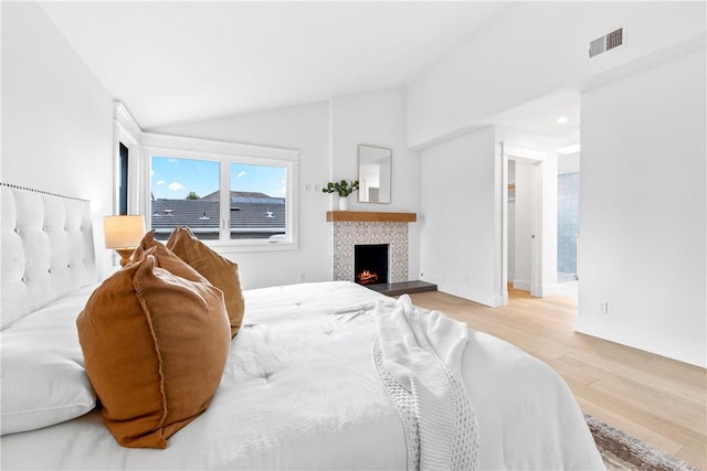 bedroom with a fireplace, visible vents, vaulted ceiling, wood finished floors, and baseboards