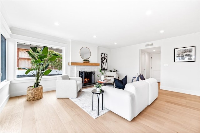 living area with a lit fireplace, light wood-type flooring, visible vents, and baseboards