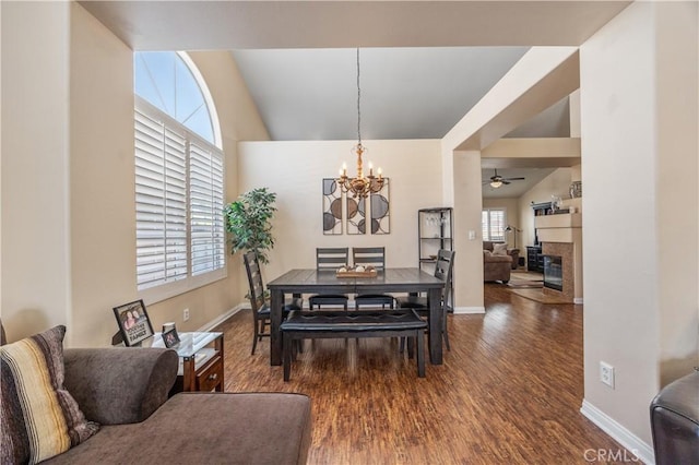 dining space with baseboards, lofted ceiling, ceiling fan with notable chandelier, a fireplace, and wood finished floors