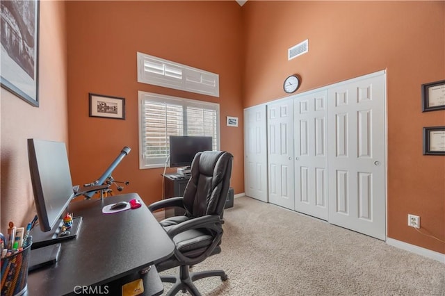 office area featuring visible vents, carpet flooring, a high ceiling, and baseboards