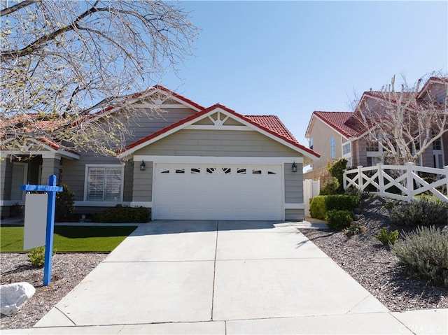 view of front of house featuring driveway, a tile roof, a garage, and fence