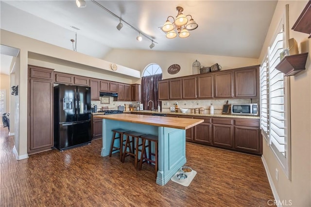 kitchen featuring wooden counters, a sink, under cabinet range hood, stainless steel microwave, and black refrigerator with ice dispenser