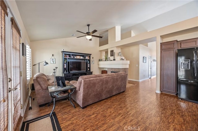 living area featuring lofted ceiling, a ceiling fan, dark wood-style floors, a fireplace, and baseboards