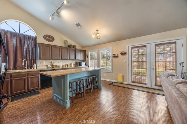 kitchen with dark wood-style floors, visible vents, vaulted ceiling, black dishwasher, and wood counters