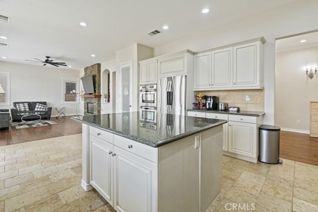 kitchen featuring stainless steel appliances, a fireplace, a kitchen island, visible vents, and a ceiling fan