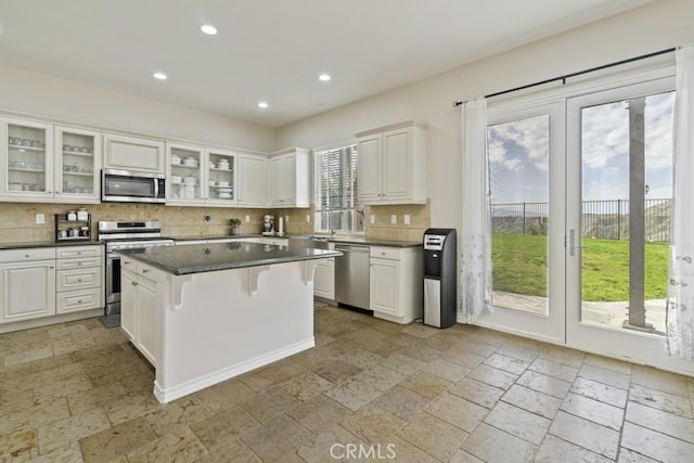 kitchen featuring a kitchen island, white cabinetry, appliances with stainless steel finishes, decorative backsplash, and dark countertops