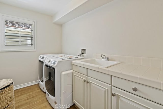 clothes washing area featuring light wood-style flooring, a sink, baseboards, washer and dryer, and cabinet space