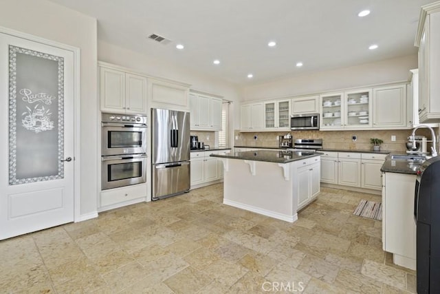 kitchen featuring tasteful backsplash, appliances with stainless steel finishes, a kitchen breakfast bar, a center island, and a sink