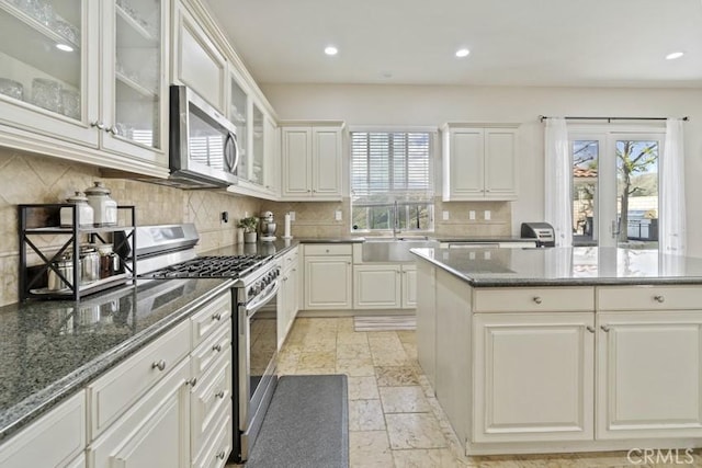 kitchen with tasteful backsplash, stone tile floors, dark stone counters, stainless steel appliances, and a sink