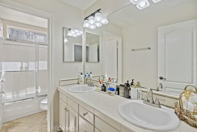 bathroom featuring toilet, double vanity, combined bath / shower with glass door, and a sink