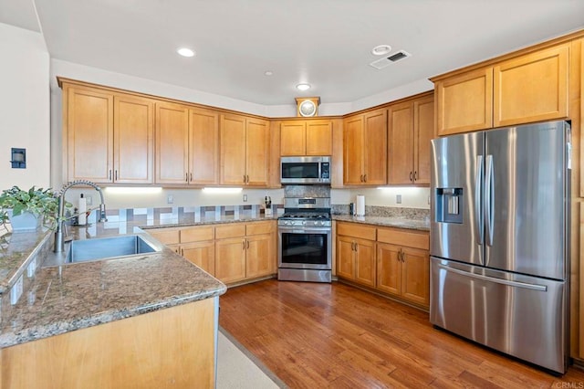 kitchen with light stone counters, stainless steel appliances, a sink, visible vents, and dark wood-style floors