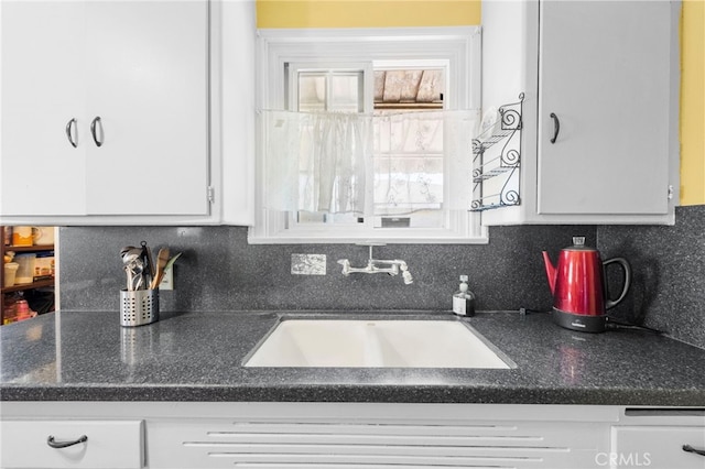 kitchen featuring plenty of natural light, white cabinetry, backsplash, and a sink