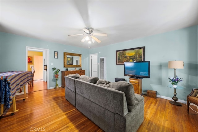 living area featuring a ceiling fan, baseboards, and wood finished floors