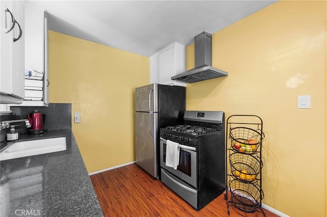 kitchen with dark wood-style floors, wall chimney exhaust hood, appliances with stainless steel finishes, white cabinetry, and a sink