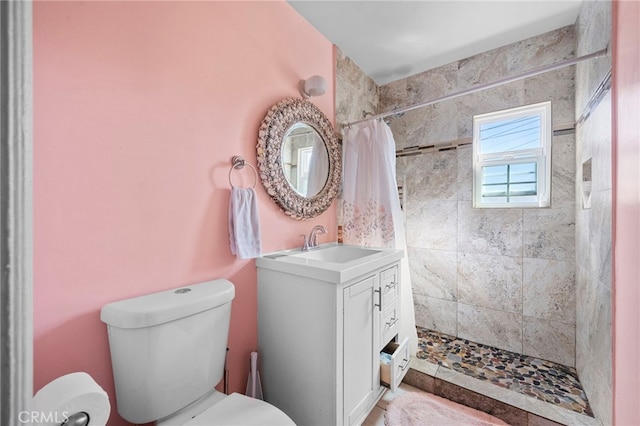 bathroom with toilet, tiled shower, and vanity