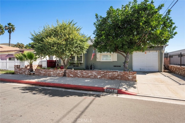 obstructed view of property featuring a garage, driveway, fence, and stucco siding