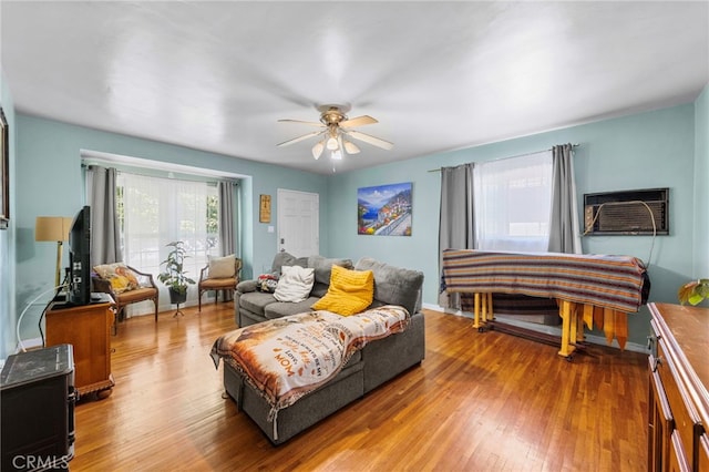 bedroom featuring a ceiling fan, an AC wall unit, baseboards, and wood finished floors