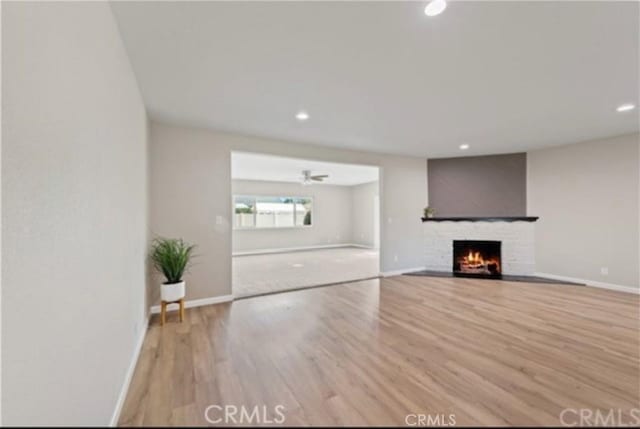 unfurnished living room featuring a ceiling fan, light wood-type flooring, a fireplace, and baseboards