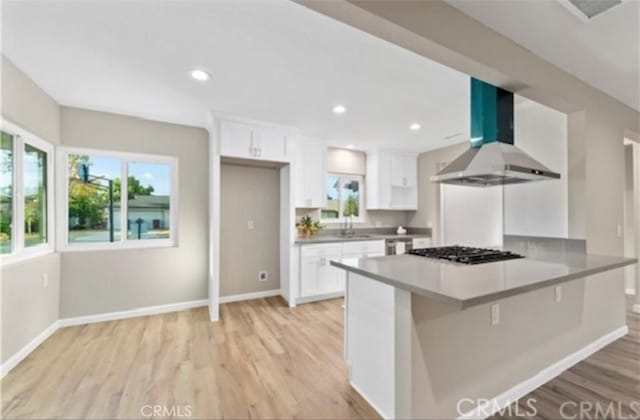 kitchen with stainless steel gas cooktop, baseboards, light wood-style floors, white cabinets, and wall chimney range hood