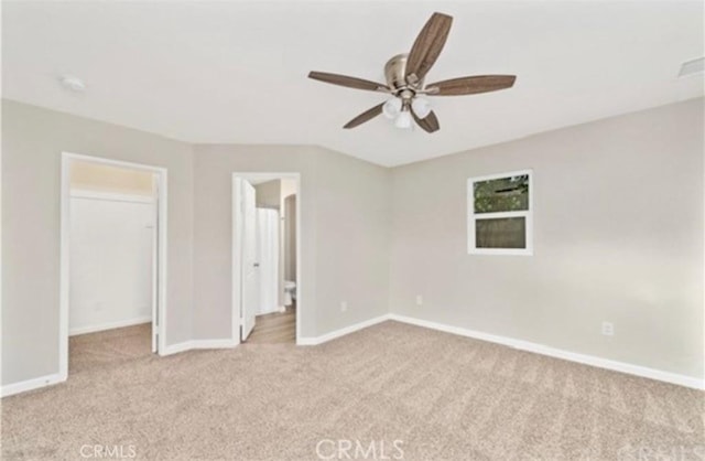 unfurnished bedroom with a walk in closet, light carpet, ceiling fan, and baseboards