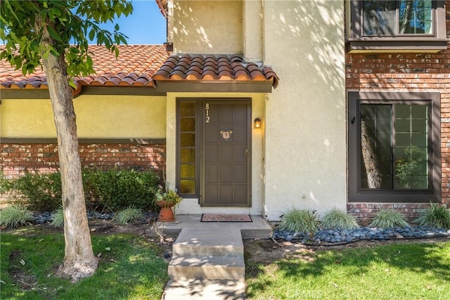 entrance to property with brick siding, a tiled roof, and stucco siding