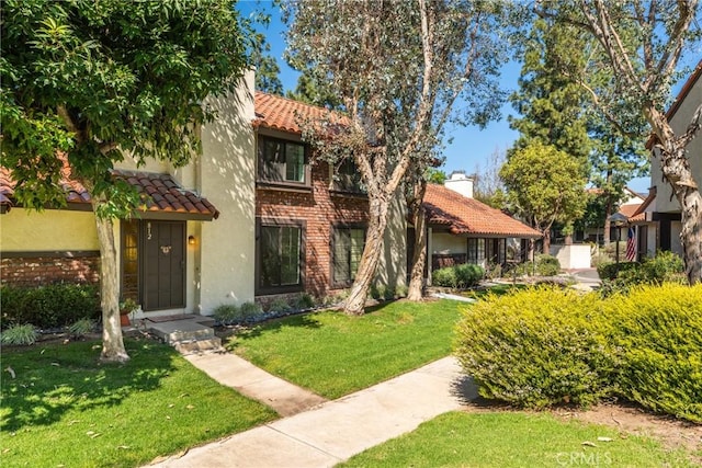 view of front of property featuring stucco siding, a chimney, a tiled roof, a front yard, and brick siding