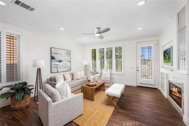 living area with a glass covered fireplace, visible vents, wood finished floors, and ornamental molding