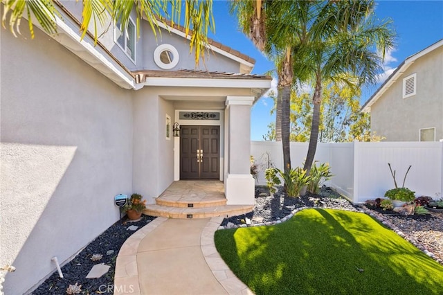 entrance to property featuring stucco siding and fence