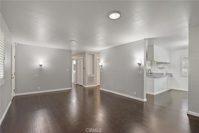 unfurnished living room with a sink, dark wood finished floors, visible vents, and baseboards