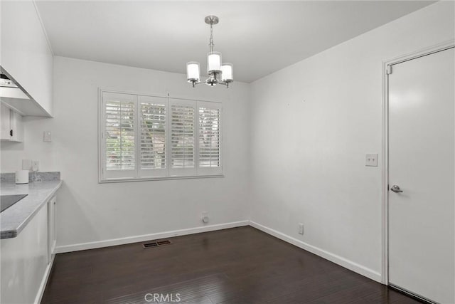 unfurnished dining area featuring an inviting chandelier, baseboards, visible vents, and dark wood-type flooring