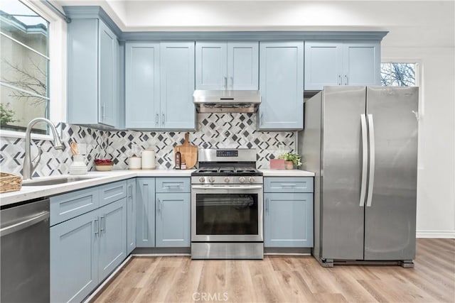 kitchen featuring light wood-style flooring, under cabinet range hood, a sink, appliances with stainless steel finishes, and light countertops