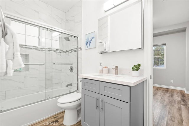 full bathroom featuring toilet, wood finished floors, combined bath / shower with glass door, baseboards, and vanity